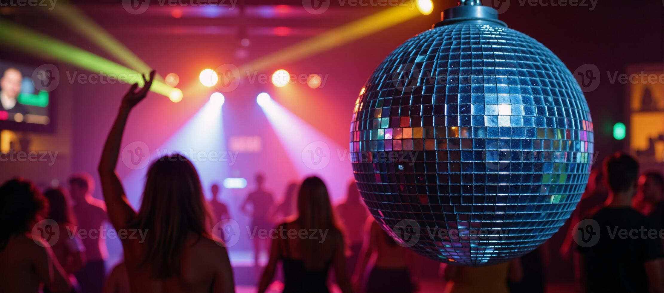 A vibrant disco ball illuminates a lively nightclub atmosphere filled with dancing and colorful lighting photo