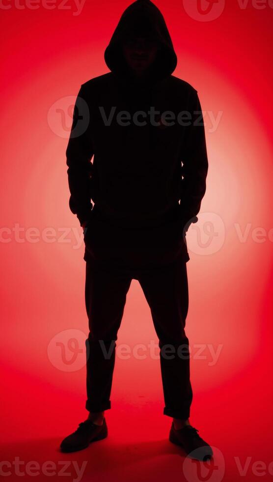 Man in hood with no visible face silhouetted against red background photo
