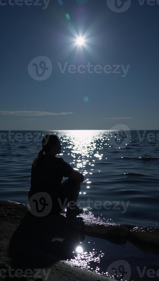 Lone figure contemplates under moonlit sky by waters edge photo