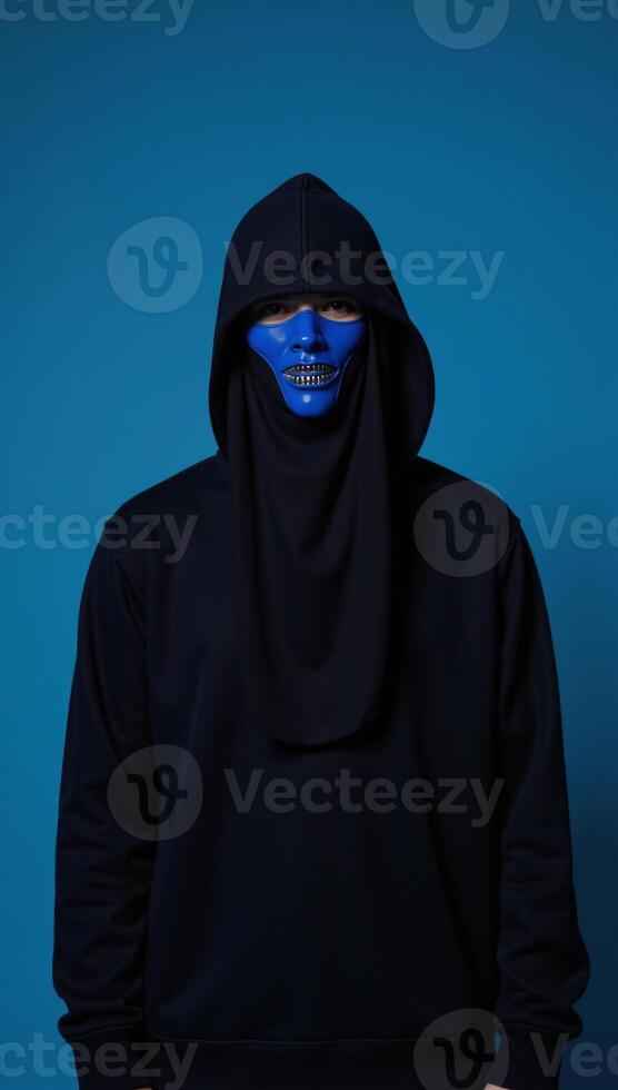 Bluemasked veiled individual with hood on blue studio backdrop photo