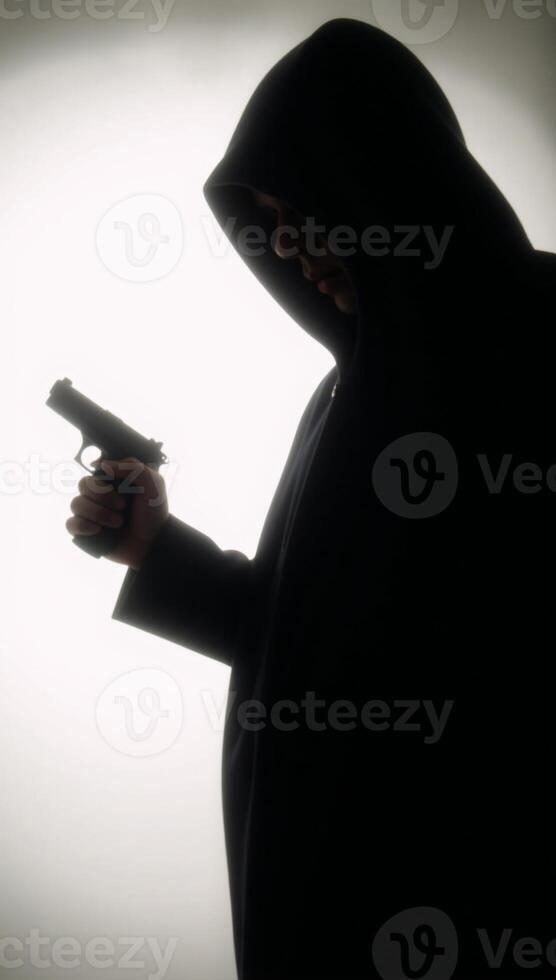 Hooded figure with gun in dark silhouette photo