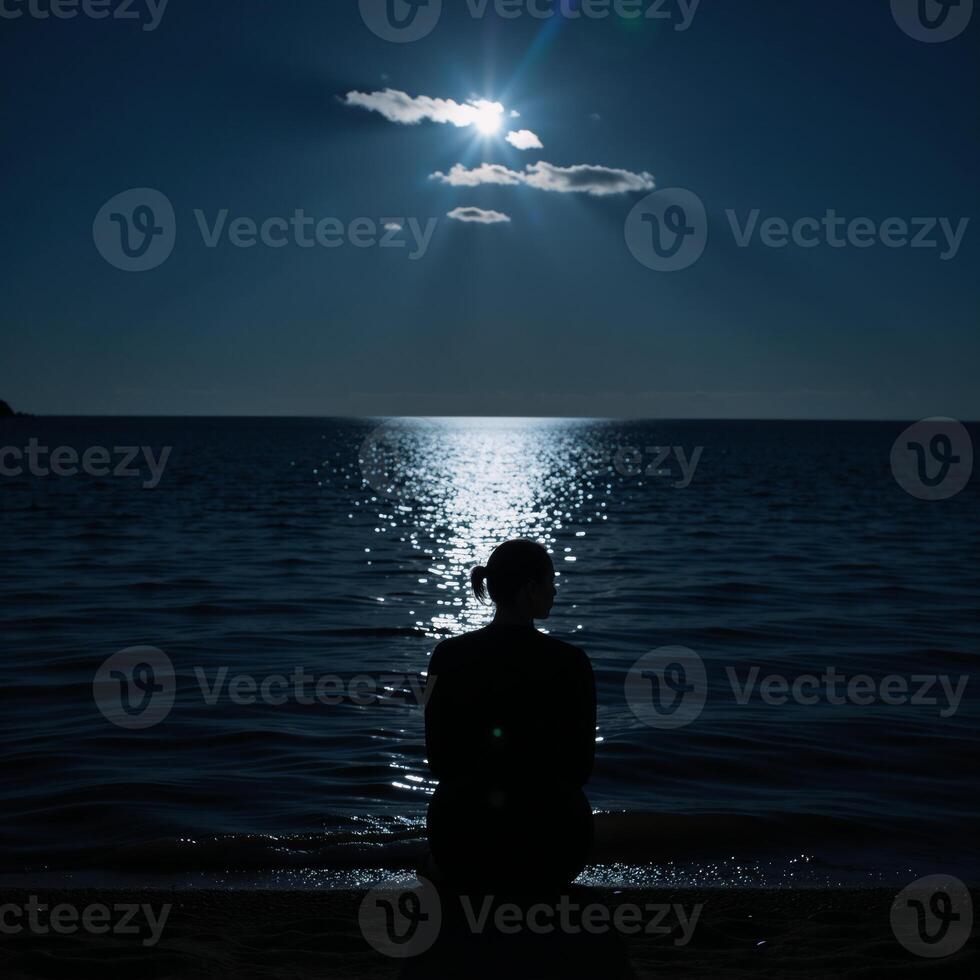 Lone figure contemplates under moonlit sky by waters edge photo