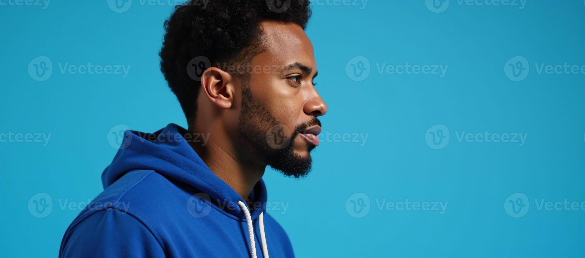 An African American man sporting an afrostyle hairdo and dressed in a hoodie stands against an isolated blue backdrop photo