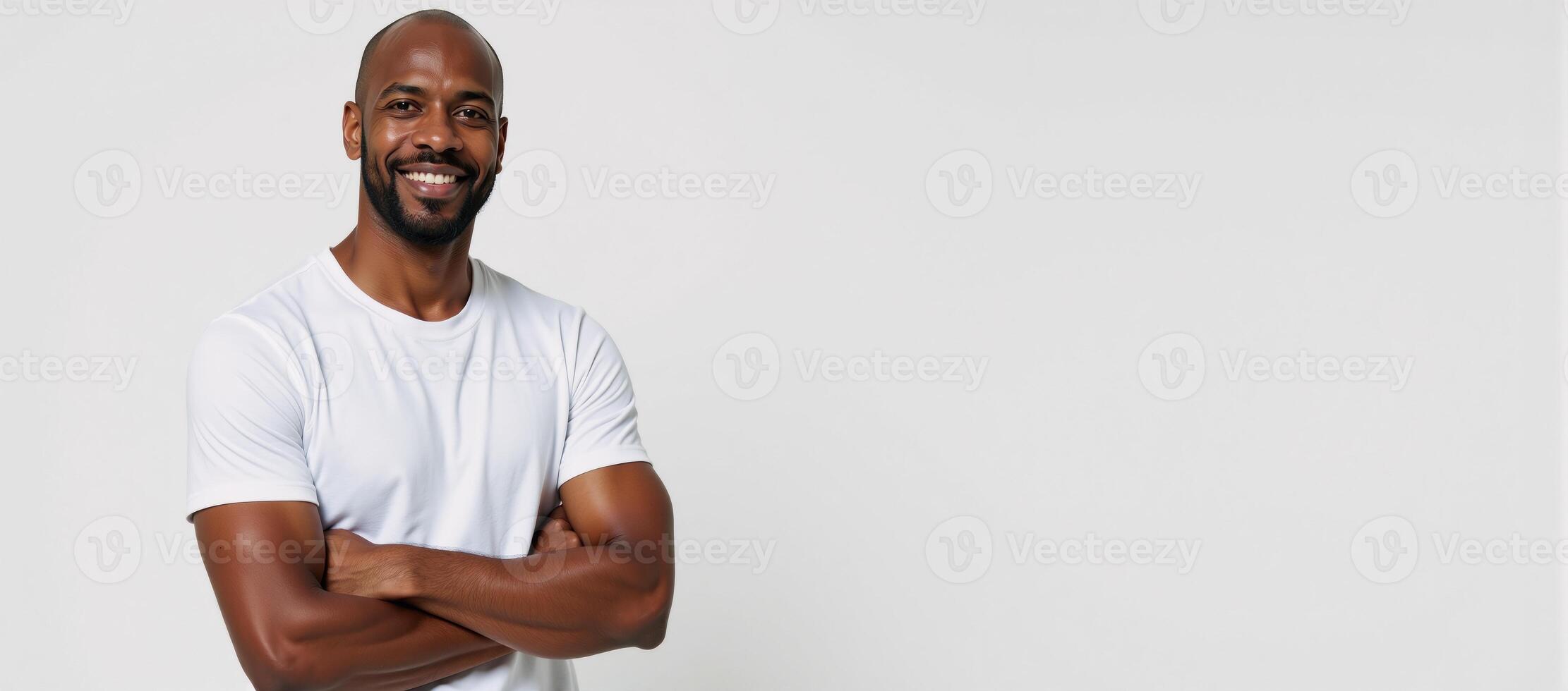 A smiling African American man poses on a white backdrop with crossed arms photo