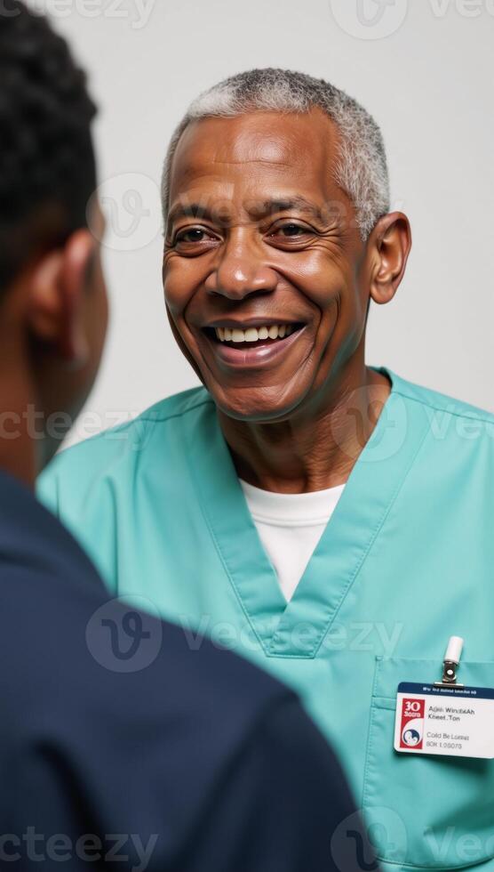 An elderly AfricanAmerican man in his 70s wears a nurses uniform and smiles joyfully sporting short white hair photo