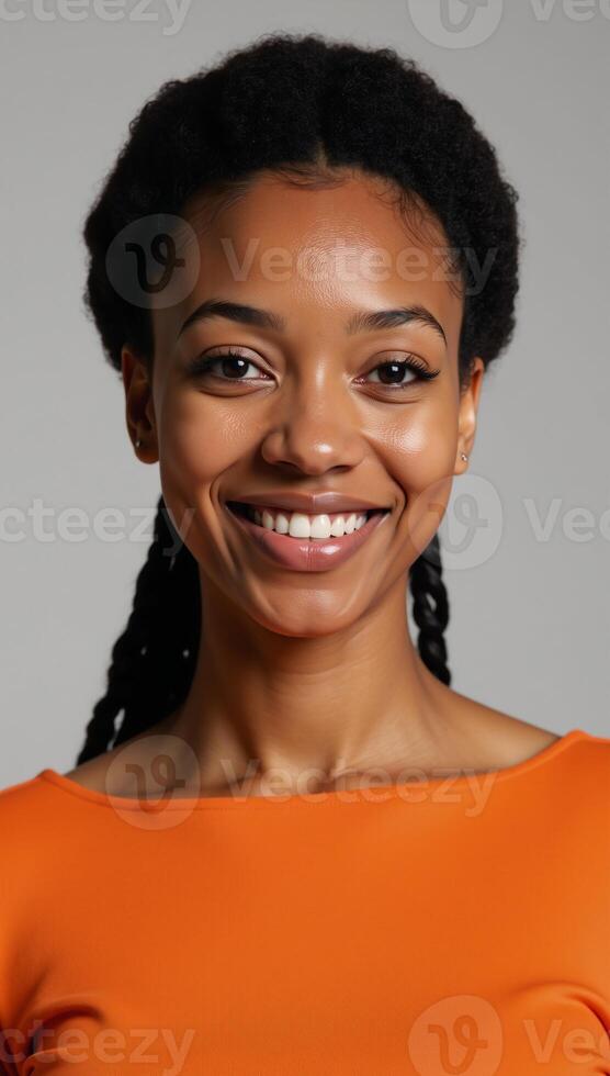 A portrait showcases an engaging smile on an African American woman donning an orange top and sporting afro braids photo