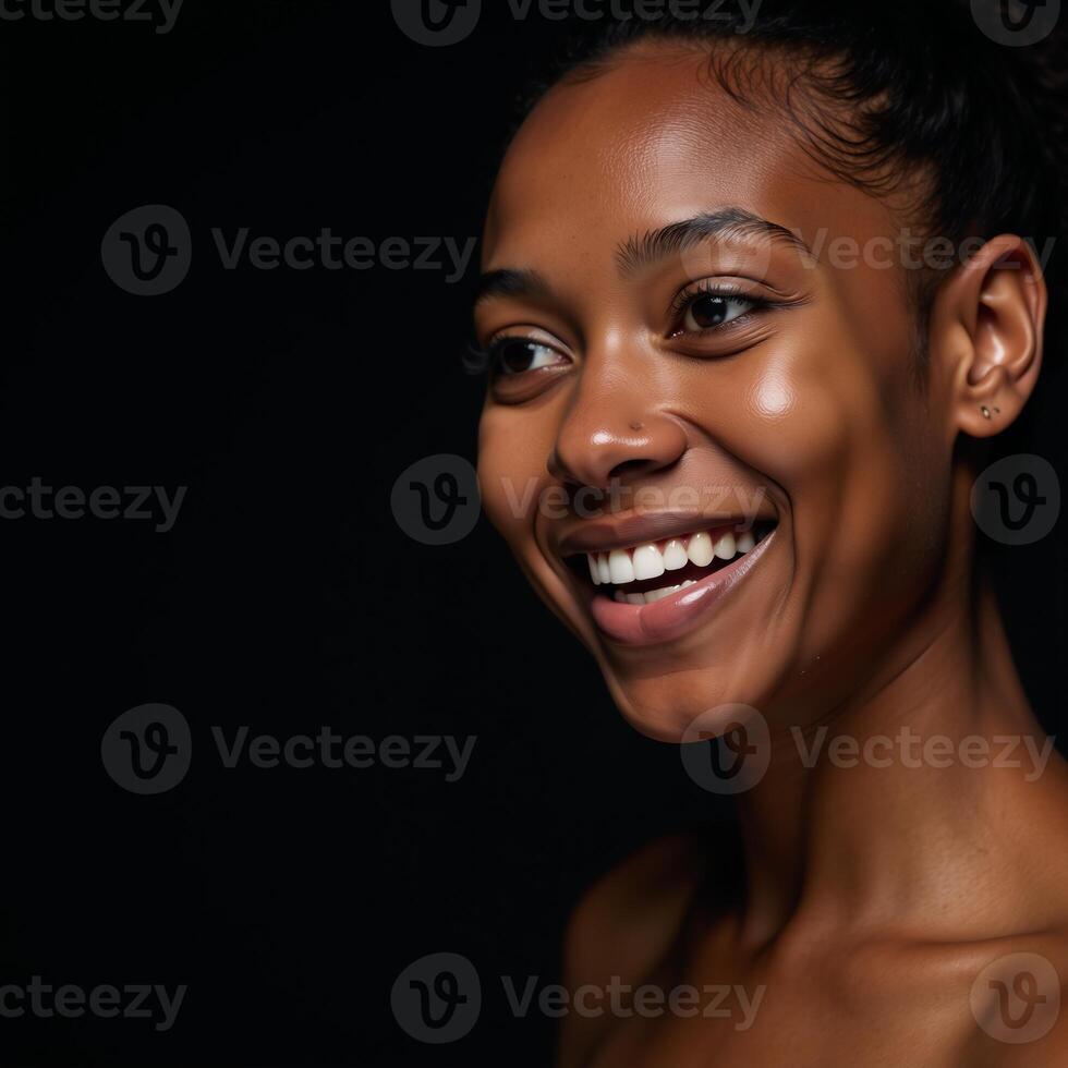 Closeup portrait of a youthful radiant African American woman with smooth skin and a bright smile gazing off into the distance on a dark backdrop photo