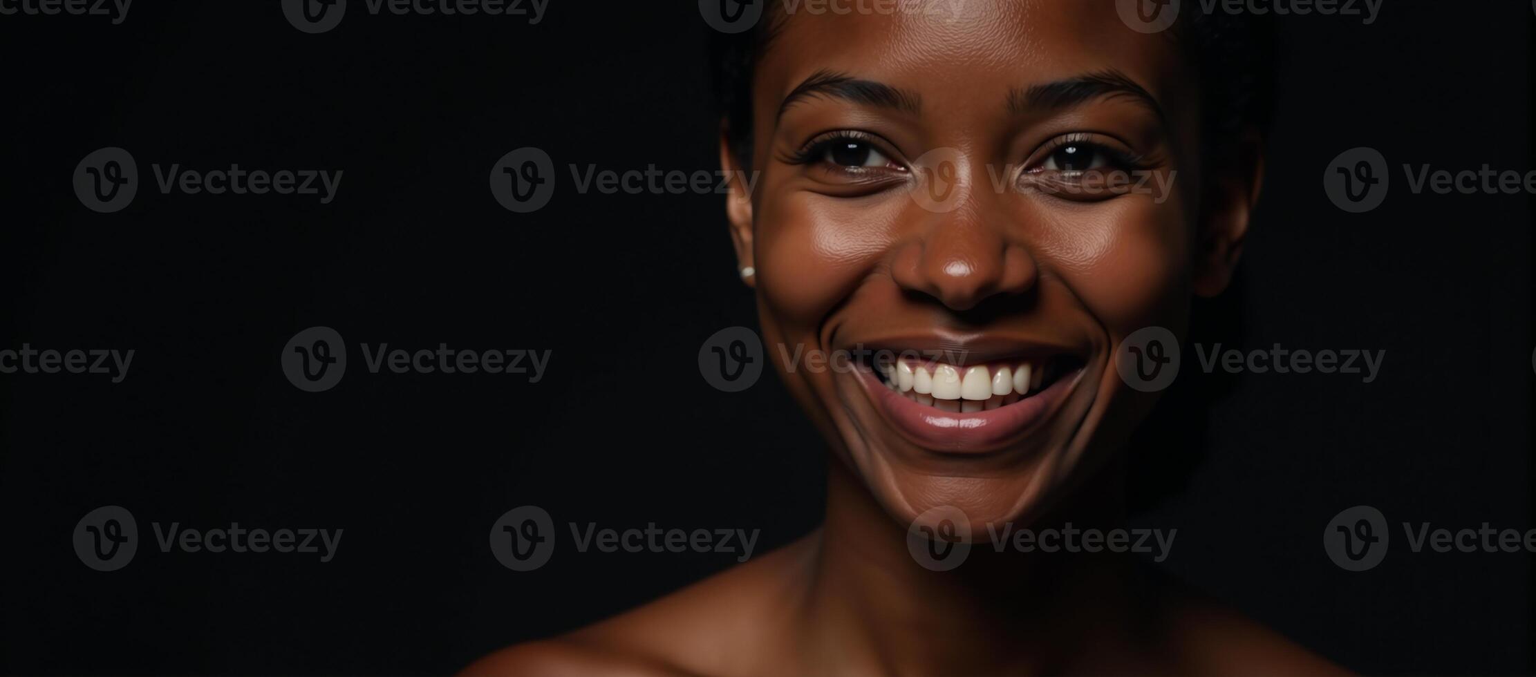 Closeup portrait of a youthful radiant African American woman with smooth skin and a bright smile gazing off into the distance on a dark backdrop photo