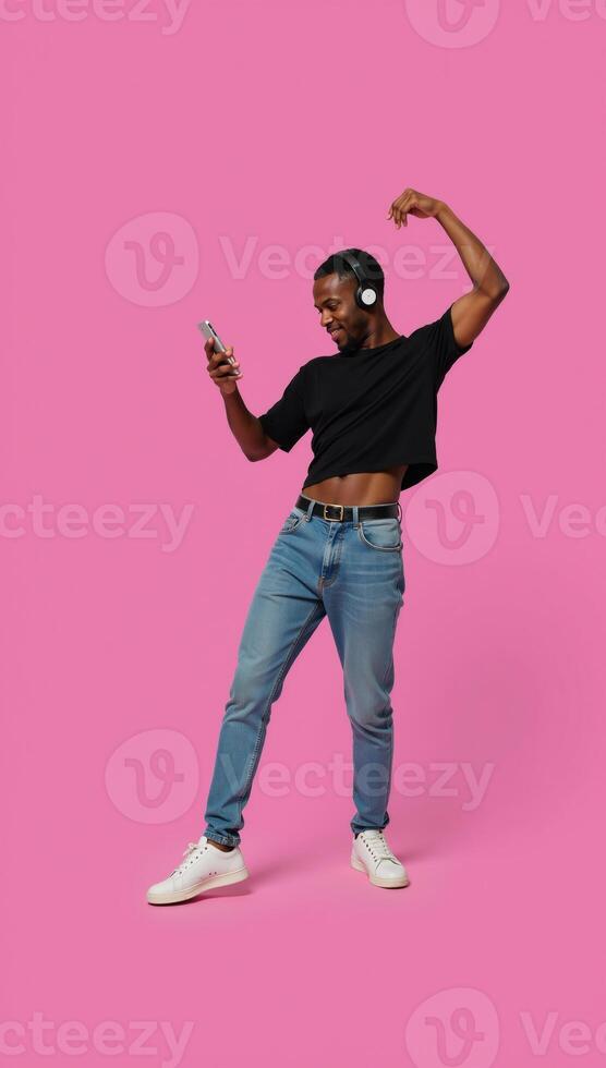 A lively generation Z AfricanAmerican man stands alone grooving to his favorite online tunes through headphones and a mobile device photo