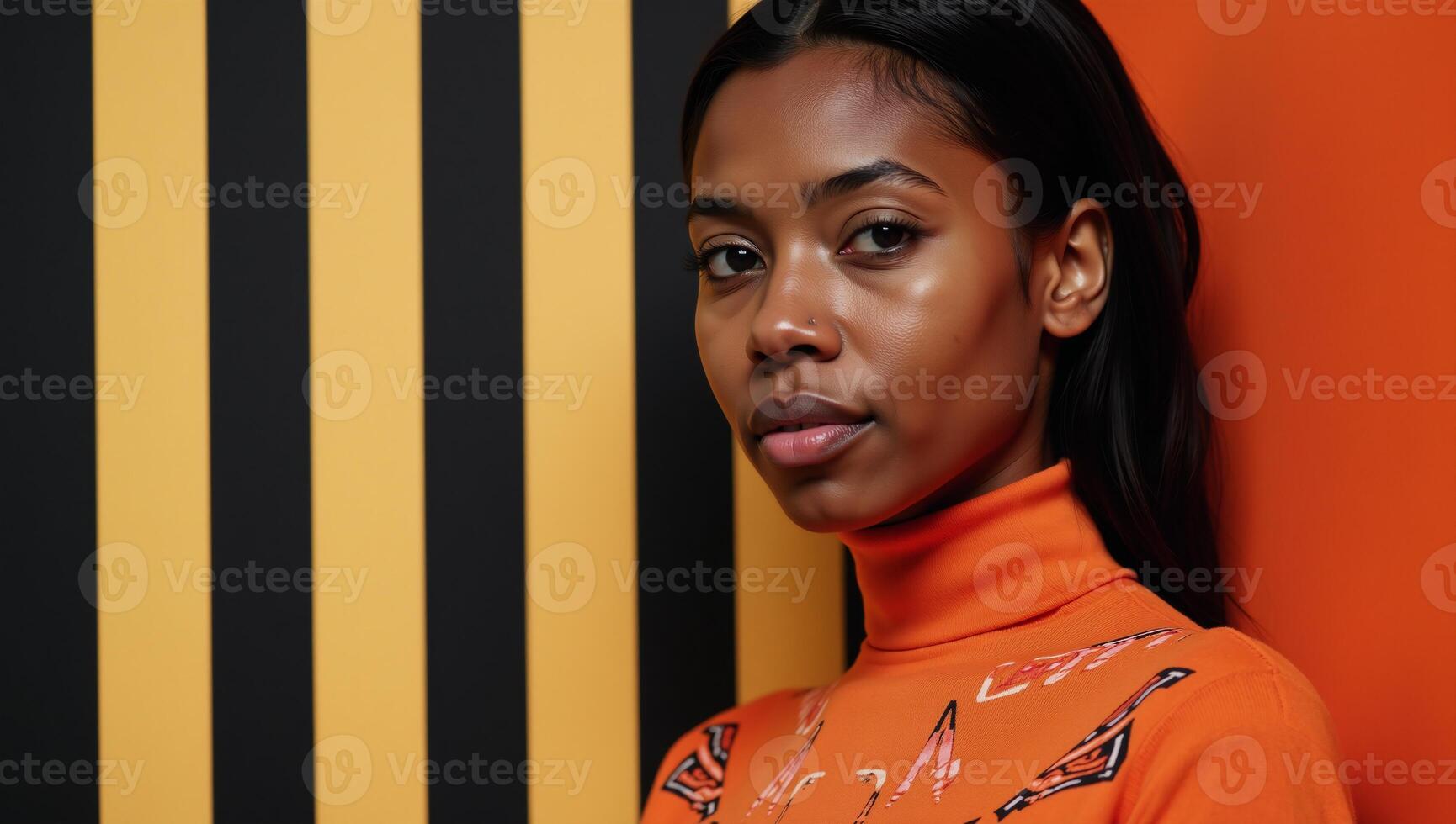 A serious AfricanAmerican female model poses in an orange turtleneck with geometric ornaments against a striped backdrop photo