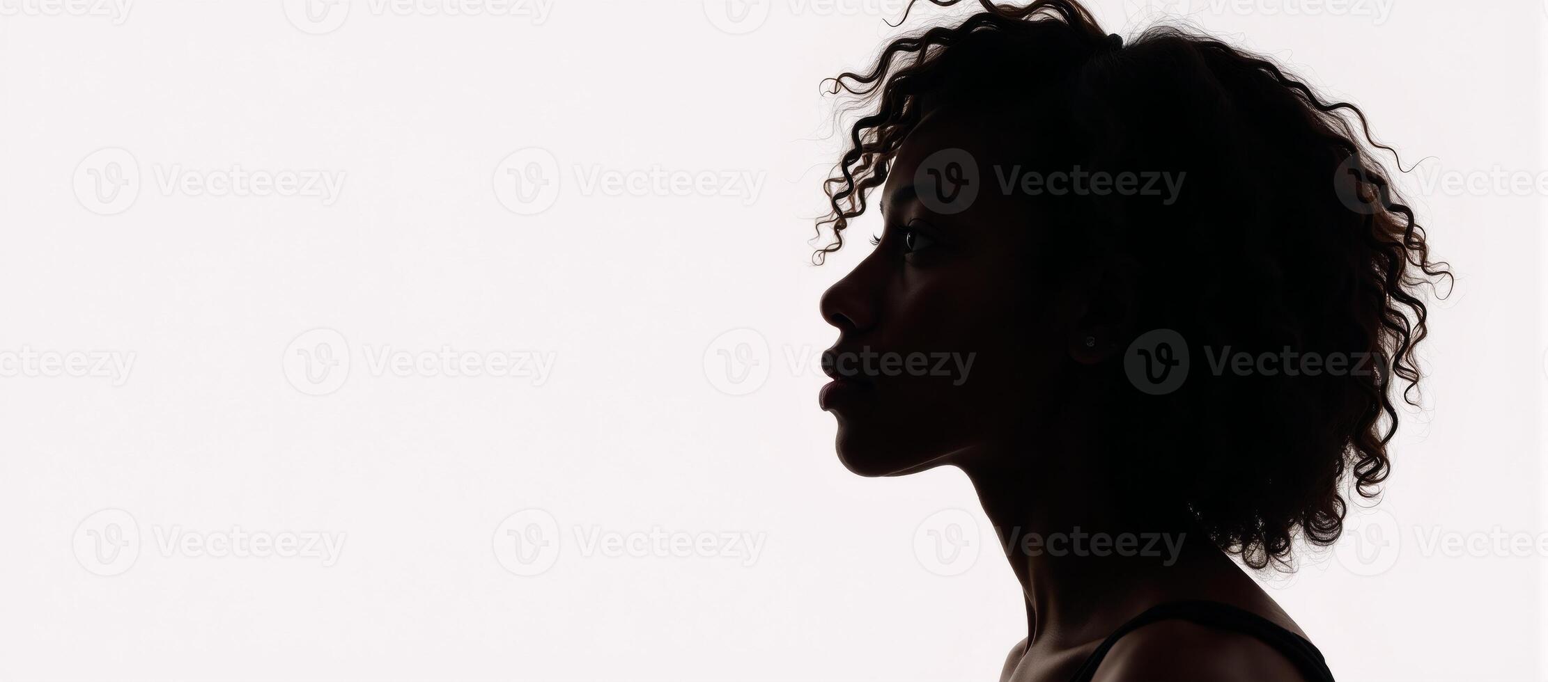 A contemplative black silhouette of an African American woman with curly hair illuminated by backlighting and gaze to the side on a white background photo