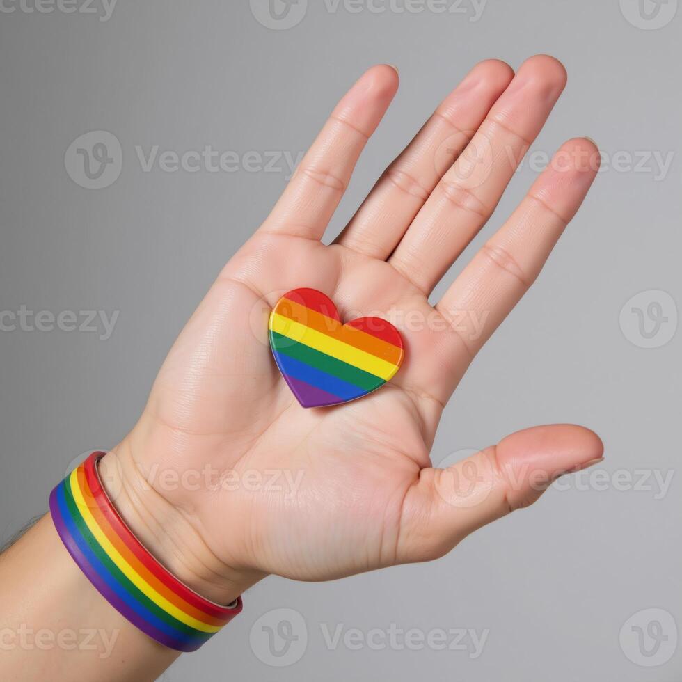 A hand wearing an LGBTQ Pride rainbowwristed band is shown against a backdrop of a heart shaped rainbow flag symbolizing Gay Pride photo
