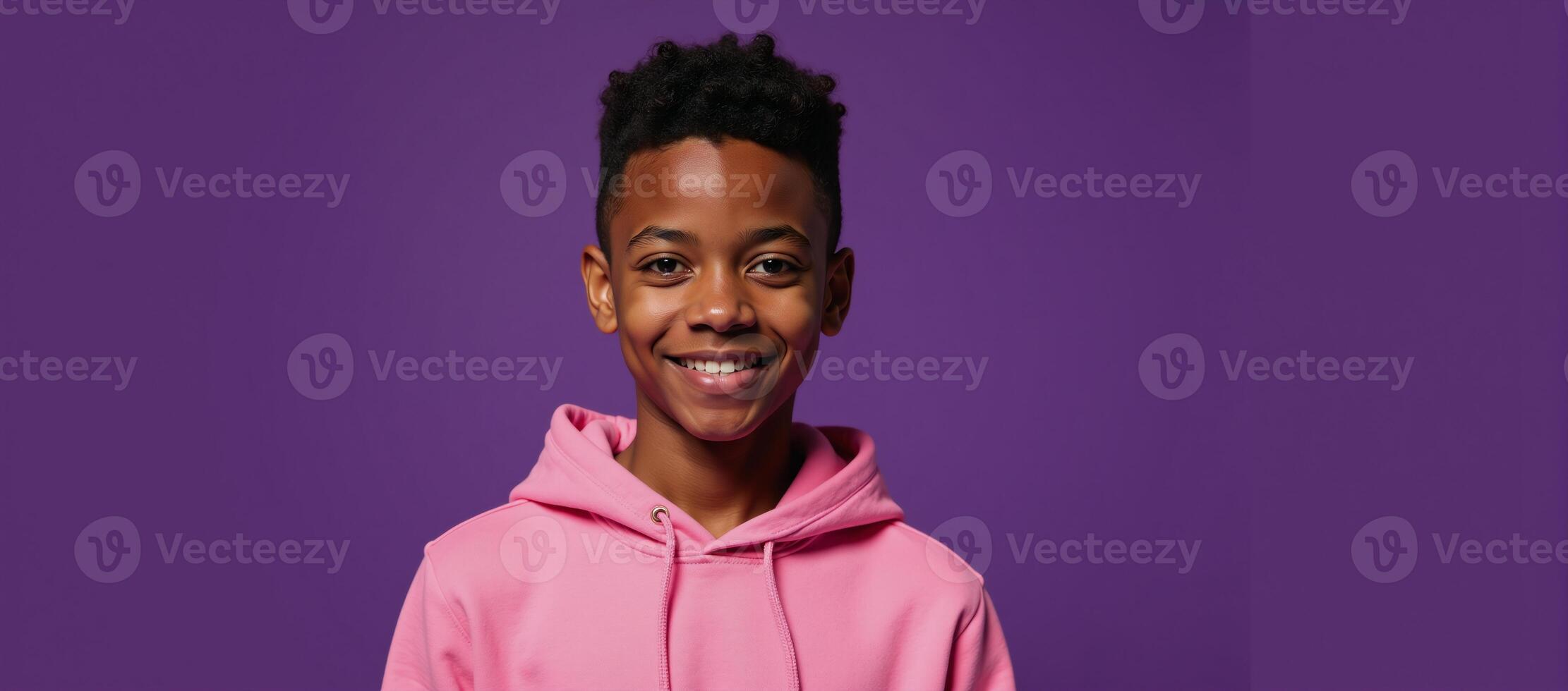 Young AfricanAmerican male in pink hoodie smiles for isolationstyle headshot on purple backdrop photo