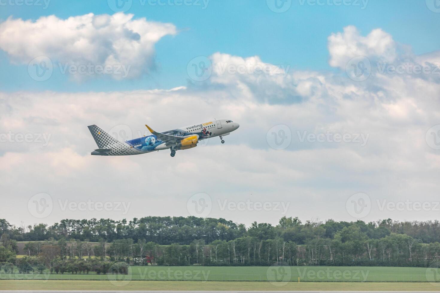 A large airplane flying over a field of green trees photo