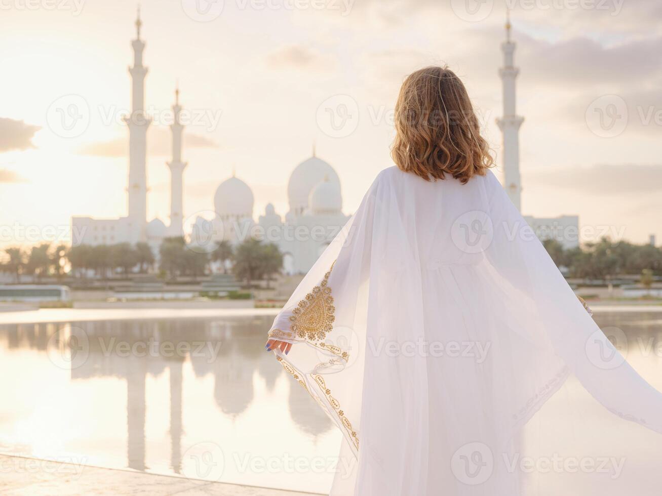 Travel to the United Arab Emirates, Abu Dhabi. Woman in white Arabic dress looking at Sheikh Zayed Great white mosque. famous Abu Dhabi sightseeing. photo