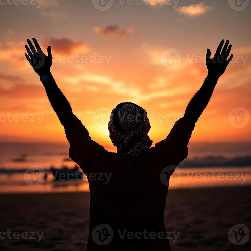 A man is standing on a beach with his hands raised in the air photo