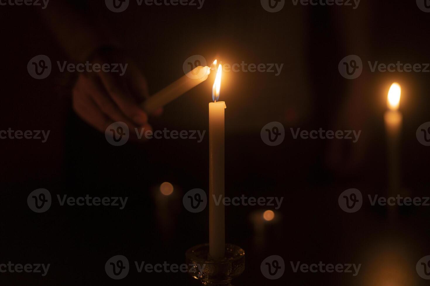 Man's hand lighting a candle in the dark against background of defocused burning candles photo