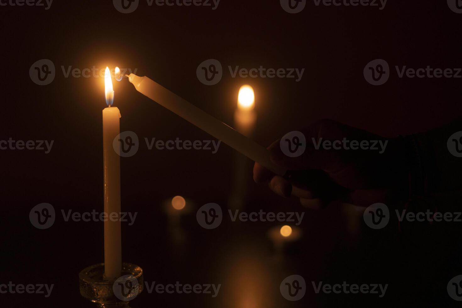 Man's hand lighting a candle in the dark against background of out-of-focus burning candles photo