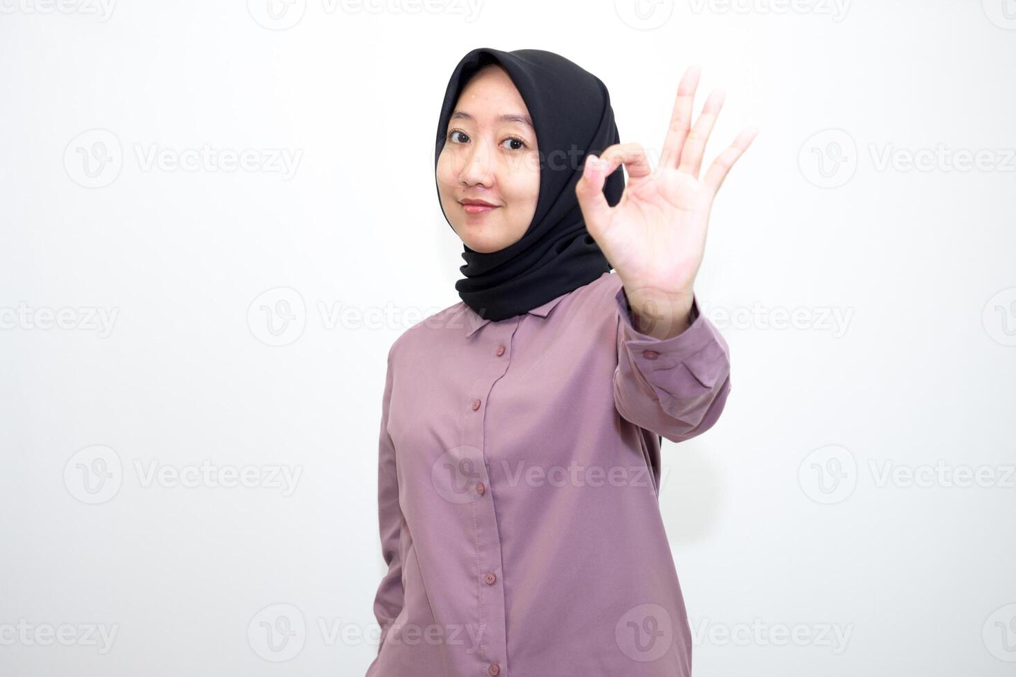 portrait of Indonesian Asian woman wearing shirt and hijab showing ok sign with one hand on eyes looking at camera through fingers. giving sign of agreement. Isolated on white Background photo