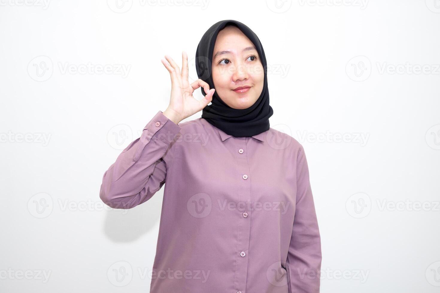 portrait of Indonesian Asian woman wearing shirt and hijab showing ok sign with one hand on eyes looking at camera through fingers. giving sign of agreement. Isolated on white Background photo