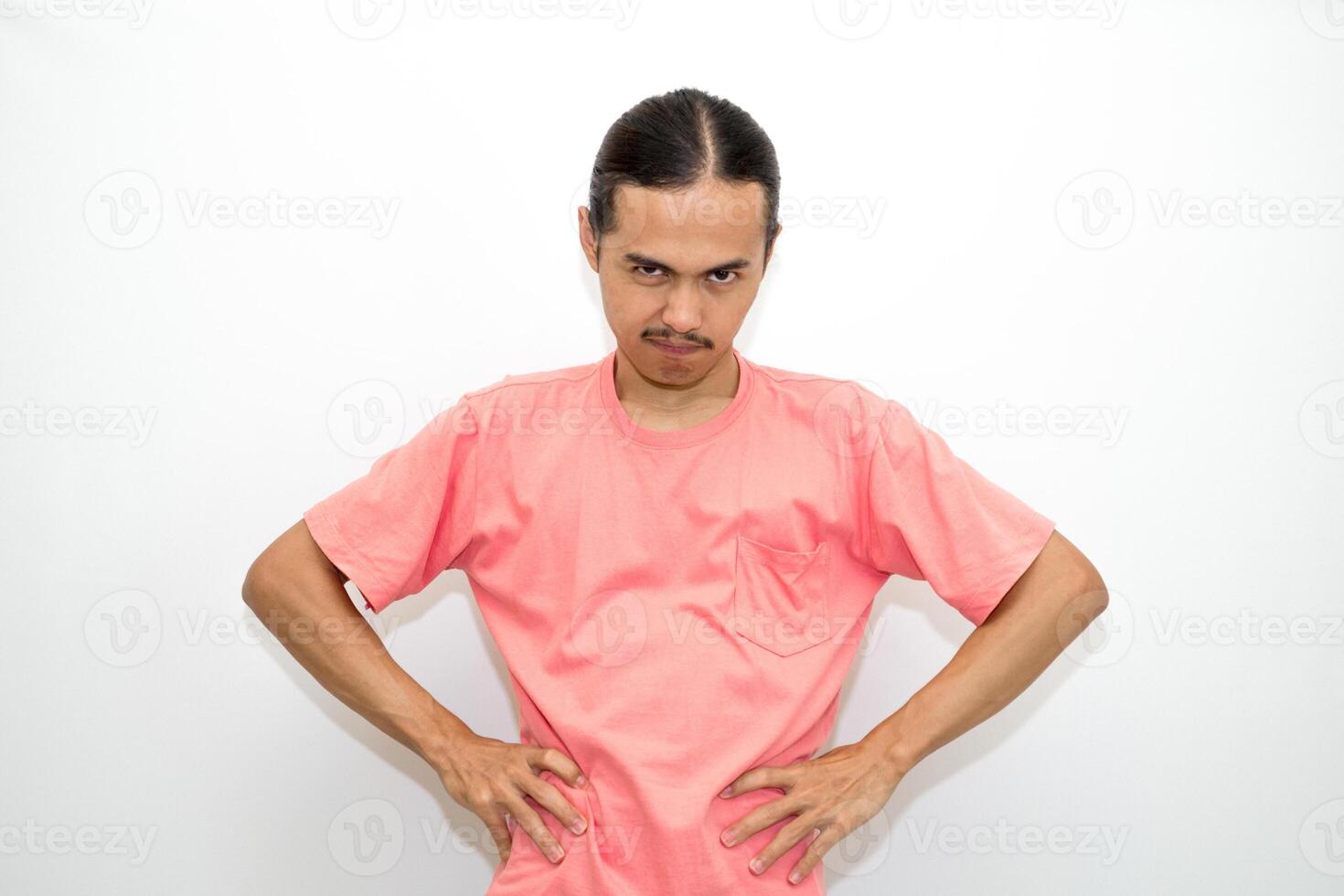 An Indonesian, Asian man wearing a pink tshirt shows a fierce expression as if he is angry or frustrated. isolated in white background photo