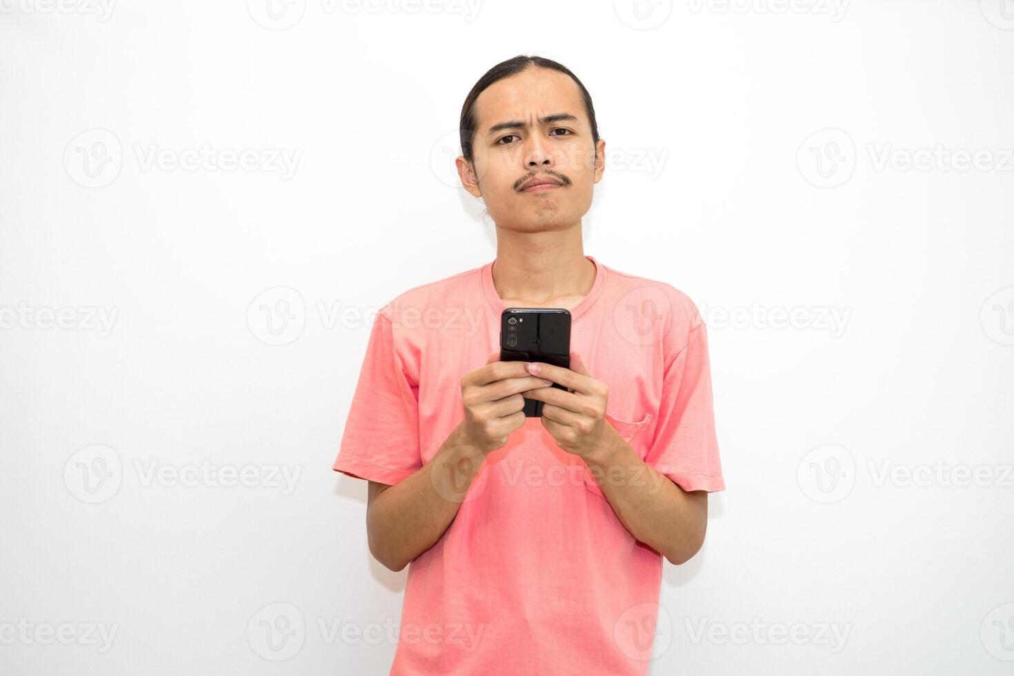 Asian, Indonesian man standing holding cellphone with hand on chin as if thinking hard, thinking about work or school assignment to find solution. Isolated on white background photo