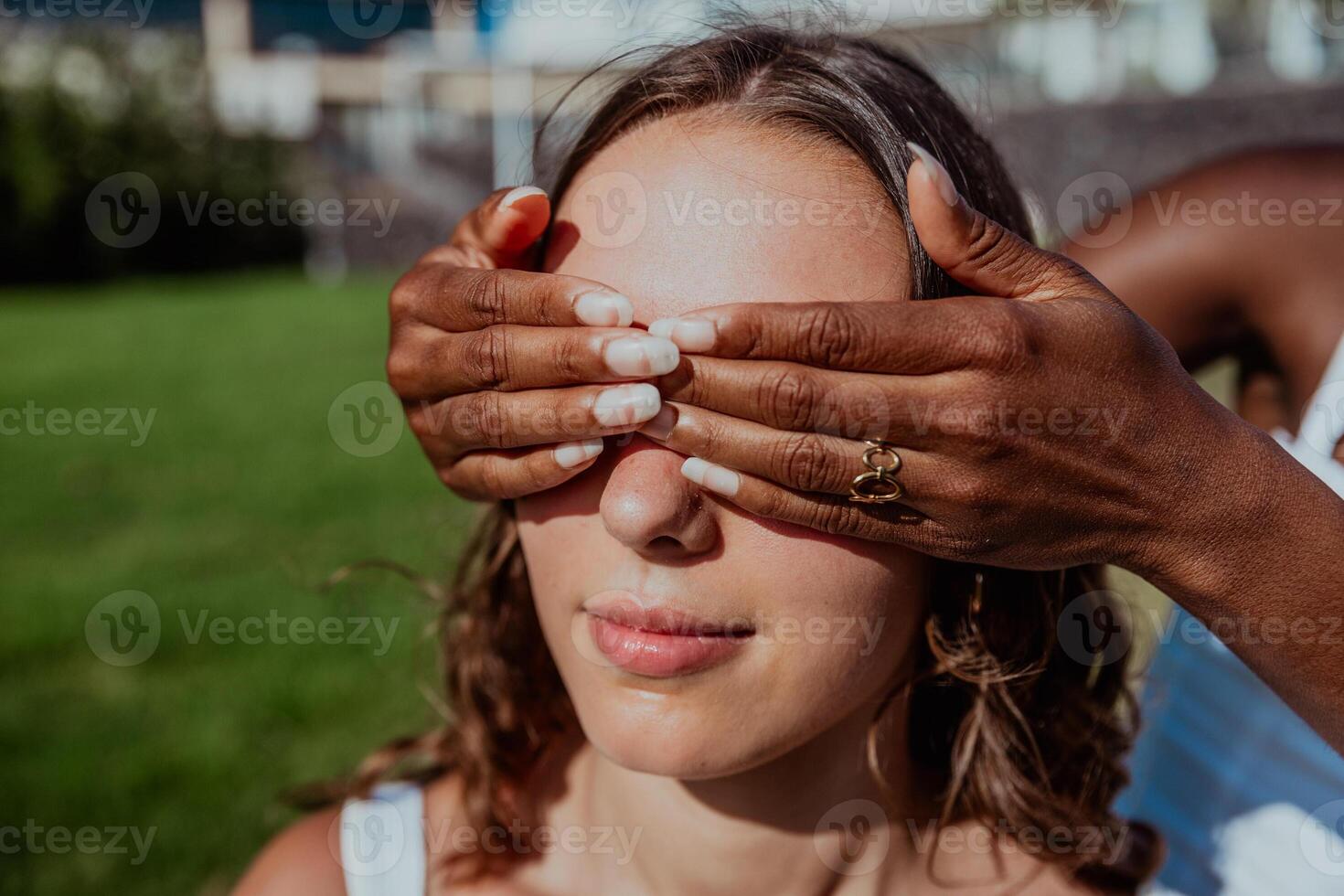A white woman has her eyes closed by her black friend's hands covering her face photo