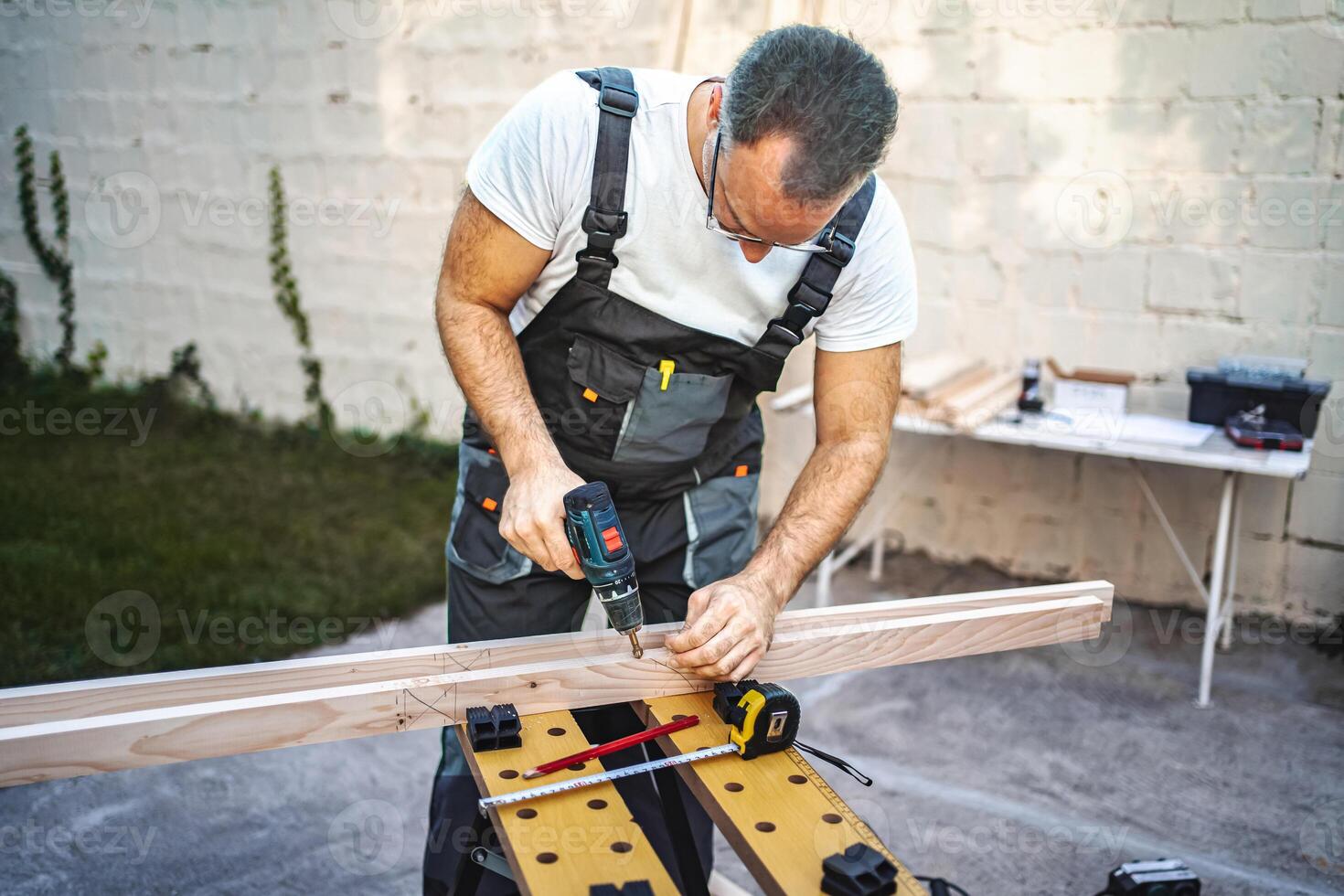 Mature male carpenter using electric drill on a wooden plank outdoors photo