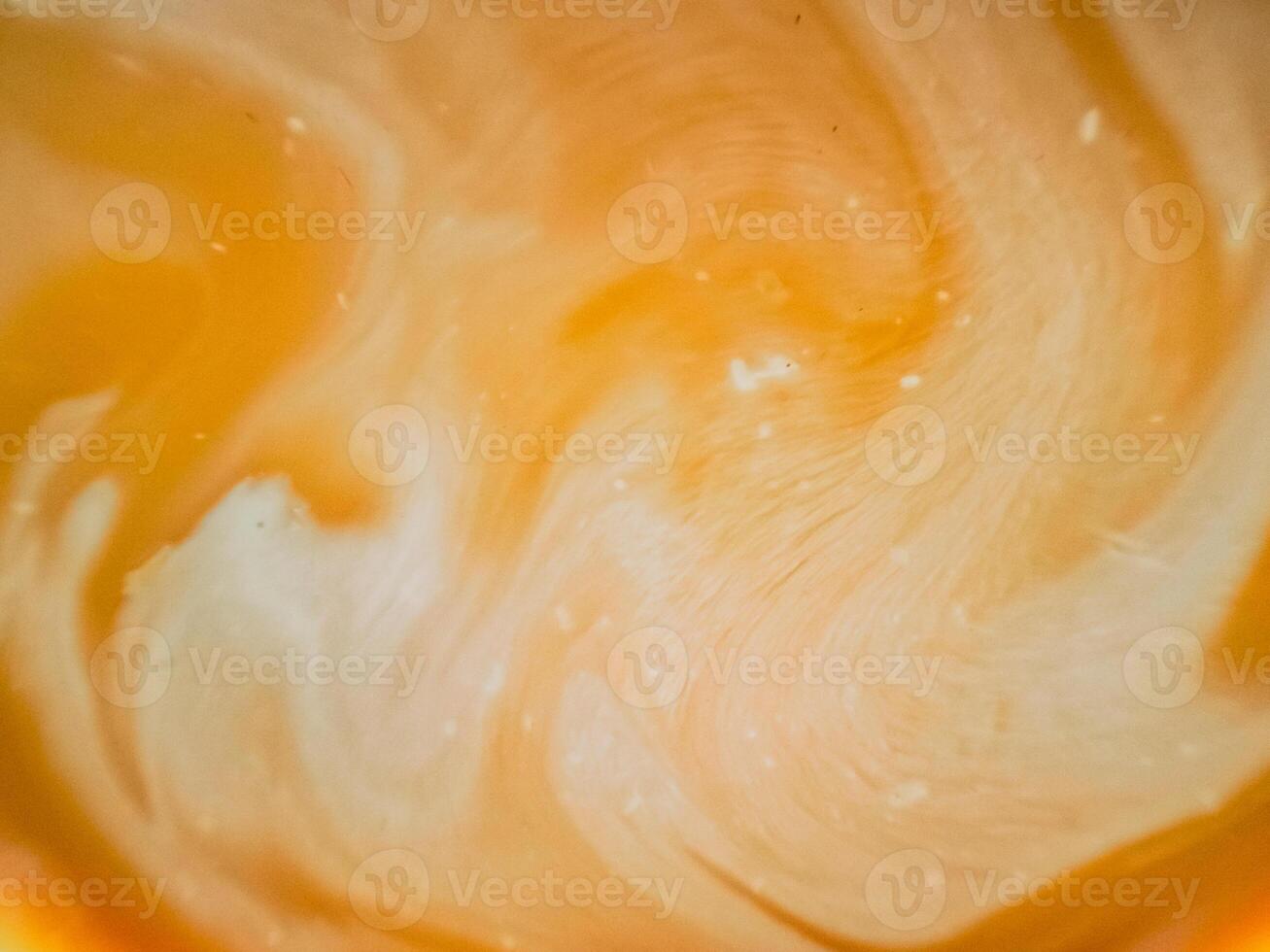 High-angle full-frame shot of coffee and milk swirling together, featuring frothy foam bubbles and creating a captivating abstract pattern. photo