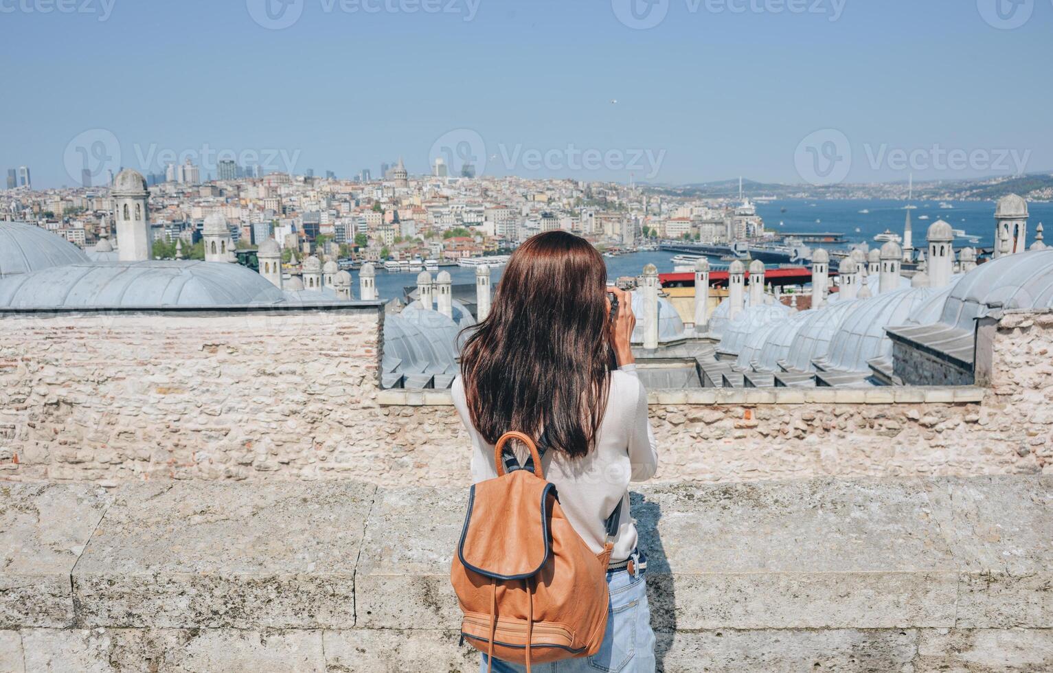 A young traveler with a backpack on her back looks at the landscape from the Suleymaniye Mosque on a sunny day in Istanbul. photo