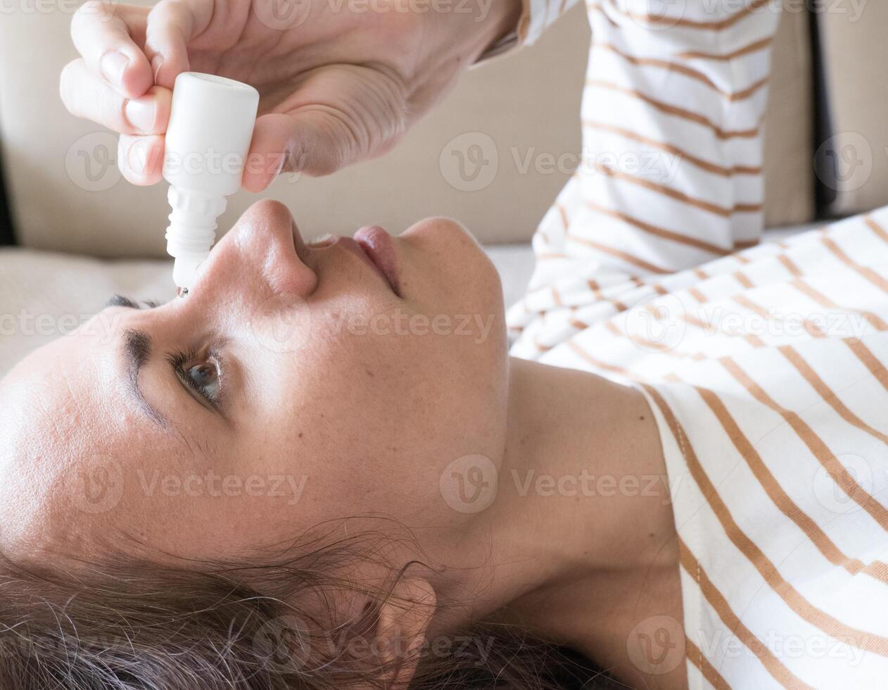 Woman dripping into her eyes with antibacterial drops closeup photo