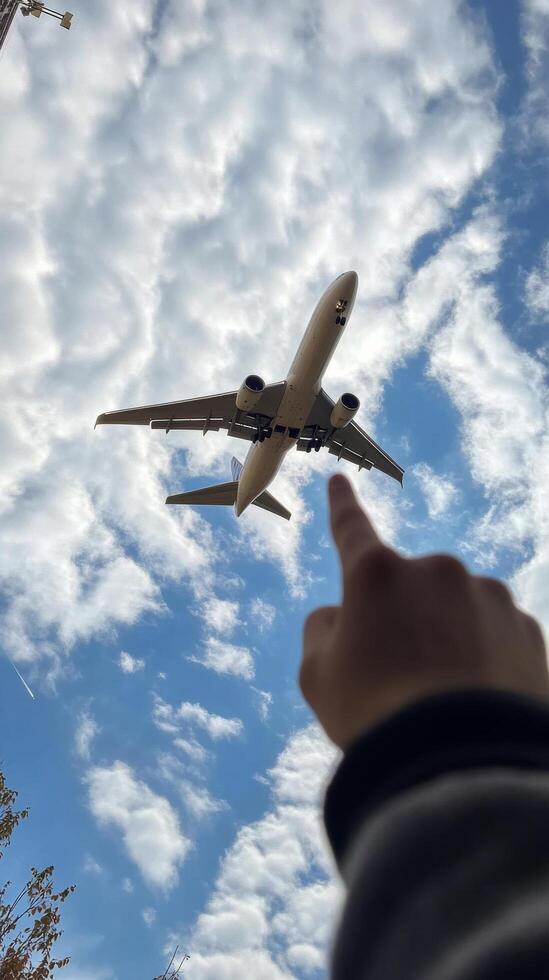 A person reaching towards a plane flying high in a clear blue sky on a sunny day photo