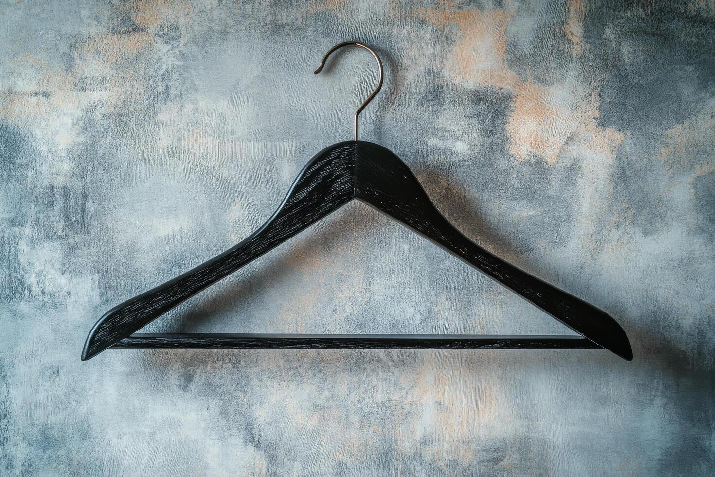 A simple black wooden hanger against a textured gray wall in a minimalist setting photo