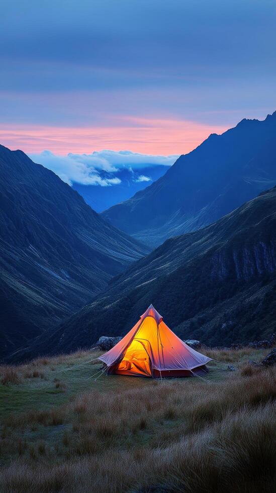 A cozy tent glows warmly in the mountains at dusk surrounded by misty peaks photo