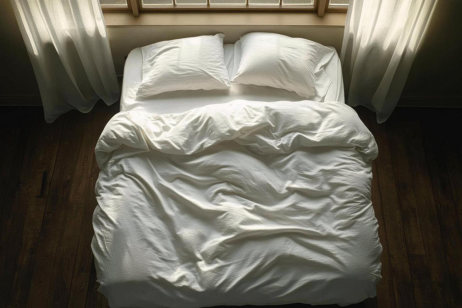 Comfortable unmade bed with white linens and pillows on wooden floor in a bright room photo
