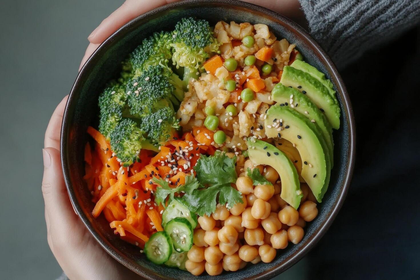 Healthy vegetarian bowl featuring fresh vegetables, chickpeas, and avocado held by hands photo