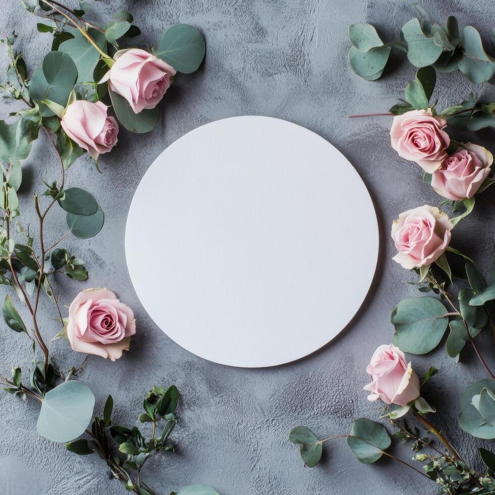 Circular blank canvas surrounded by pink roses and greenery on a textured gray surface photo