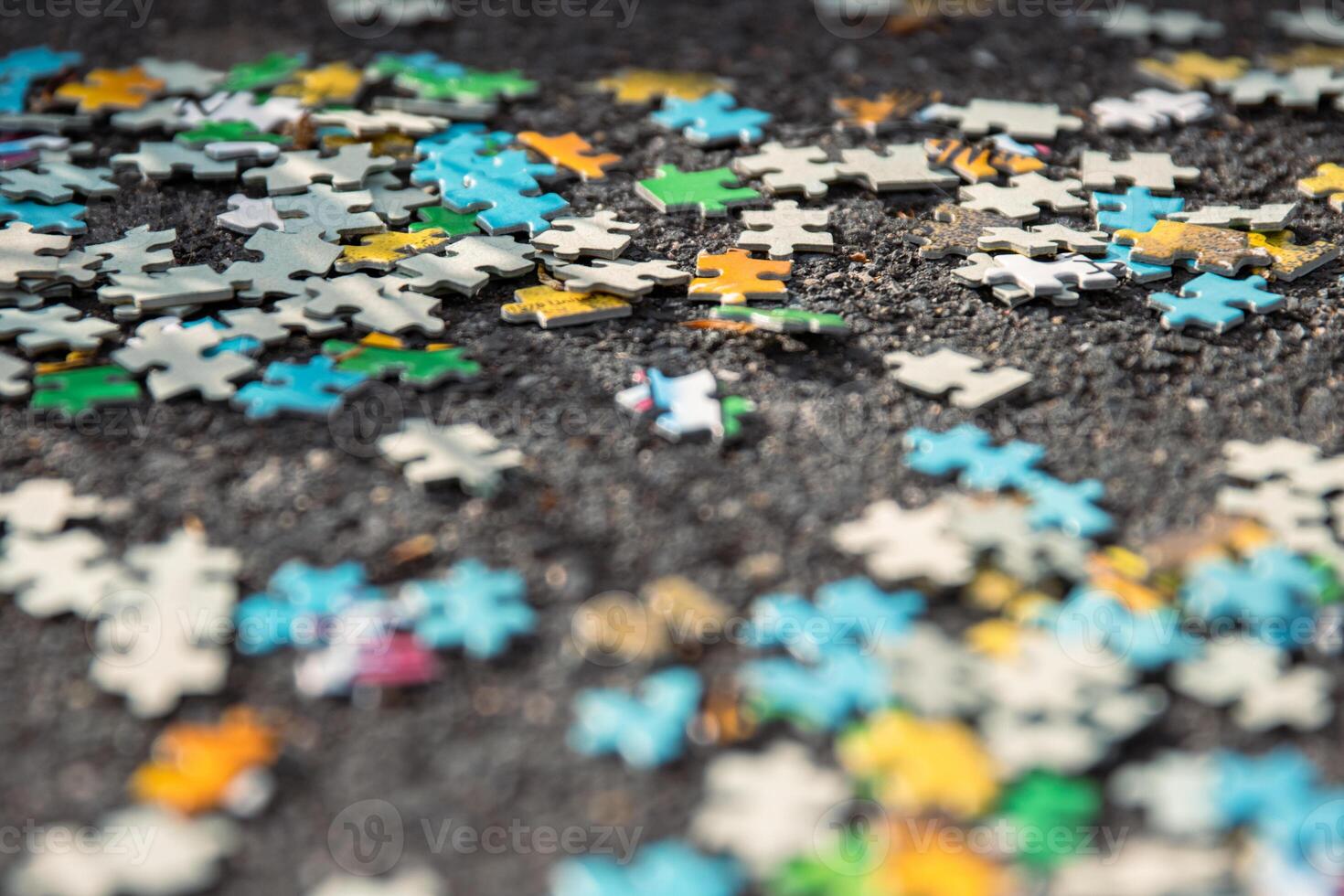 Colorful jigsaw. Unfinished scattered puzzle pieces spread on the gray asphalt pavement on the street. Messy chaotic concept. Close up. Selective focus. Blurred. photo