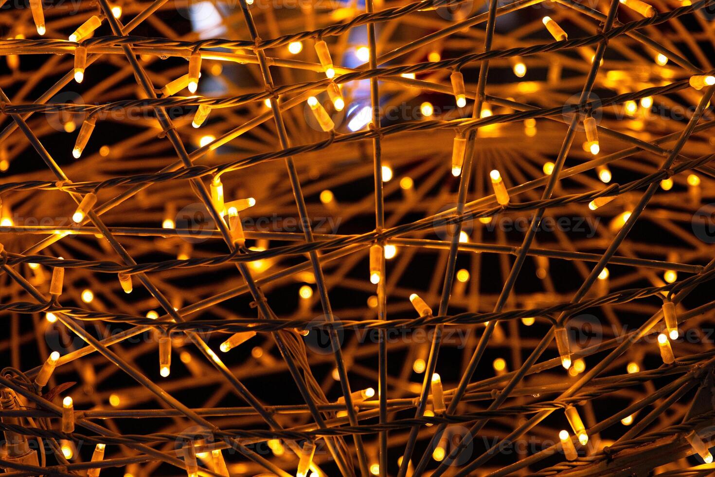 Closeup of intertwined golden string lights. Abstract view of crisscrossing glowing yellow LED garland with small bright bulbs, radiating soft golden light against a dark background. Berlin, Germany photo