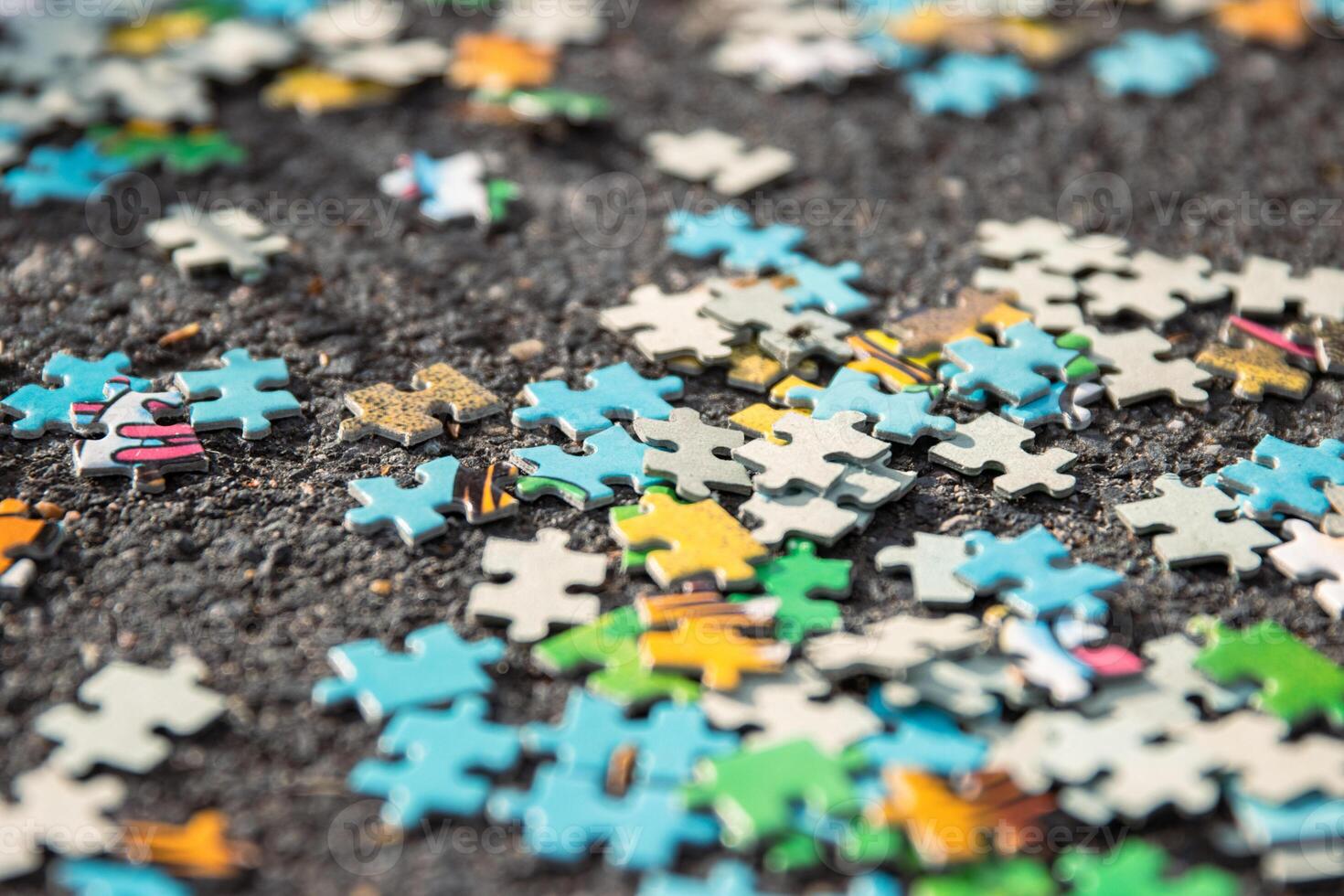 Colorful jigsaw. Unfinished scattered puzzle pieces spread on the gray asphalt pavement on the street. Messy chaotic concept. Close up. Selective focus. Blurred. photo