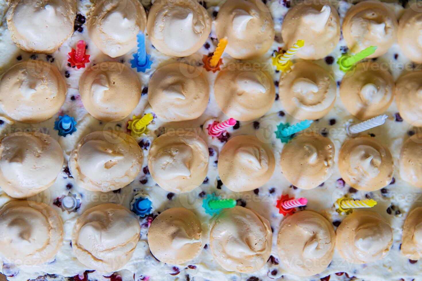 Overhead view of a colorful festive cake covered with whipped cream and topped with meringue drops and colorful birthday candles. Vibrant dessert for 15th anniversary celebration photo