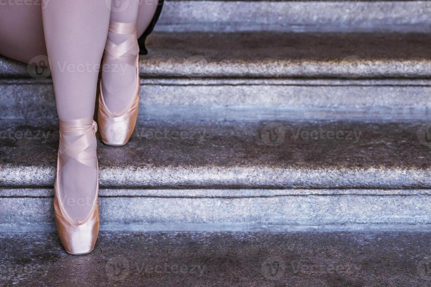 Ballerina in pink pointe shoes and white stockings sitting on stone steps capturing balance, grace, and calm. Closeup of dancer feet showing graceful ballet posture. photo