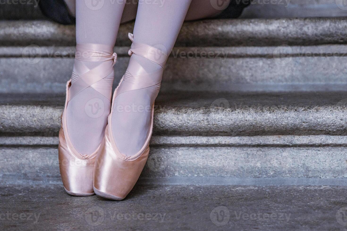 Ballerina in pink pointe shoes and white stockings sitting on stone steps capturing balance, grace, and calm. Closeup of dancer feet showing graceful ballet posture. photo