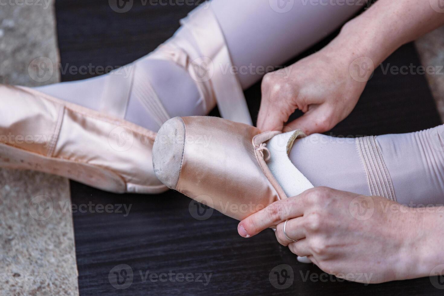 Closeup of a ballerina sitting on the floor, adjusting pointe shoe pads for foot protection during the dance. Ballet dancer putting on toe pads on her feet before performing photo