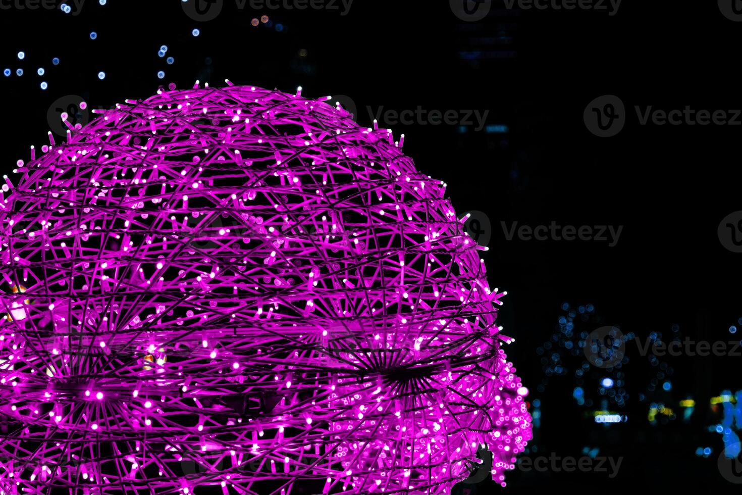 Closeup of intertwined pink magenta purple lilac neon string lights next to Christmas market. Crisscrossing glowing LED garland with small bright bulbs against dark background. Copy space photo