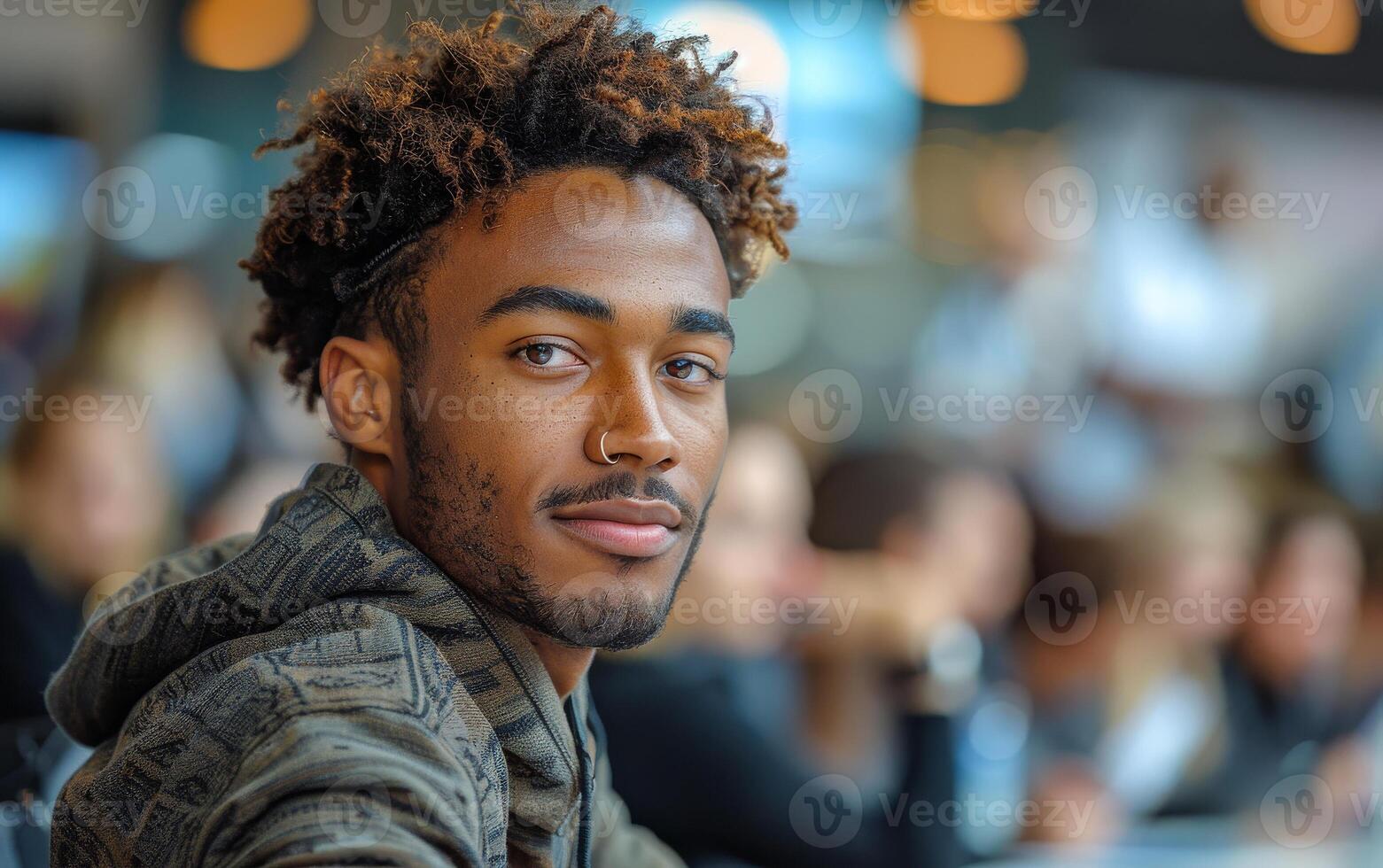 Young man engaging with a crowd in a busy venue A young man looks at the camera with a friendly expression while surrounded by a bustling group of people in a lively atmosphere. photo