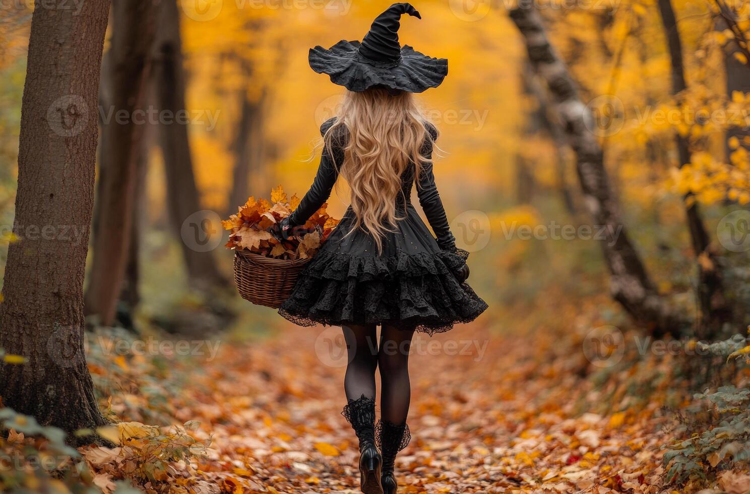 A witch gathering autumn leaves in a forest. A woman in a witch costume collects colorful autumn leaves in a serene forest filled with golden foliage. photo