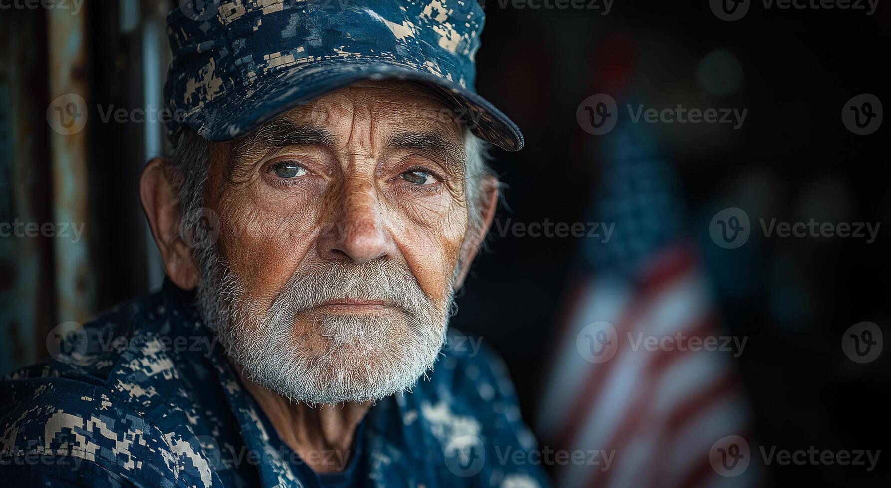 A man with a military hat and beard is standing in front of an American flag. He looks tired and sad photo