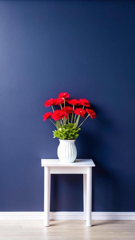 A vase of red flowers sits on a table in front of a blue wall photo