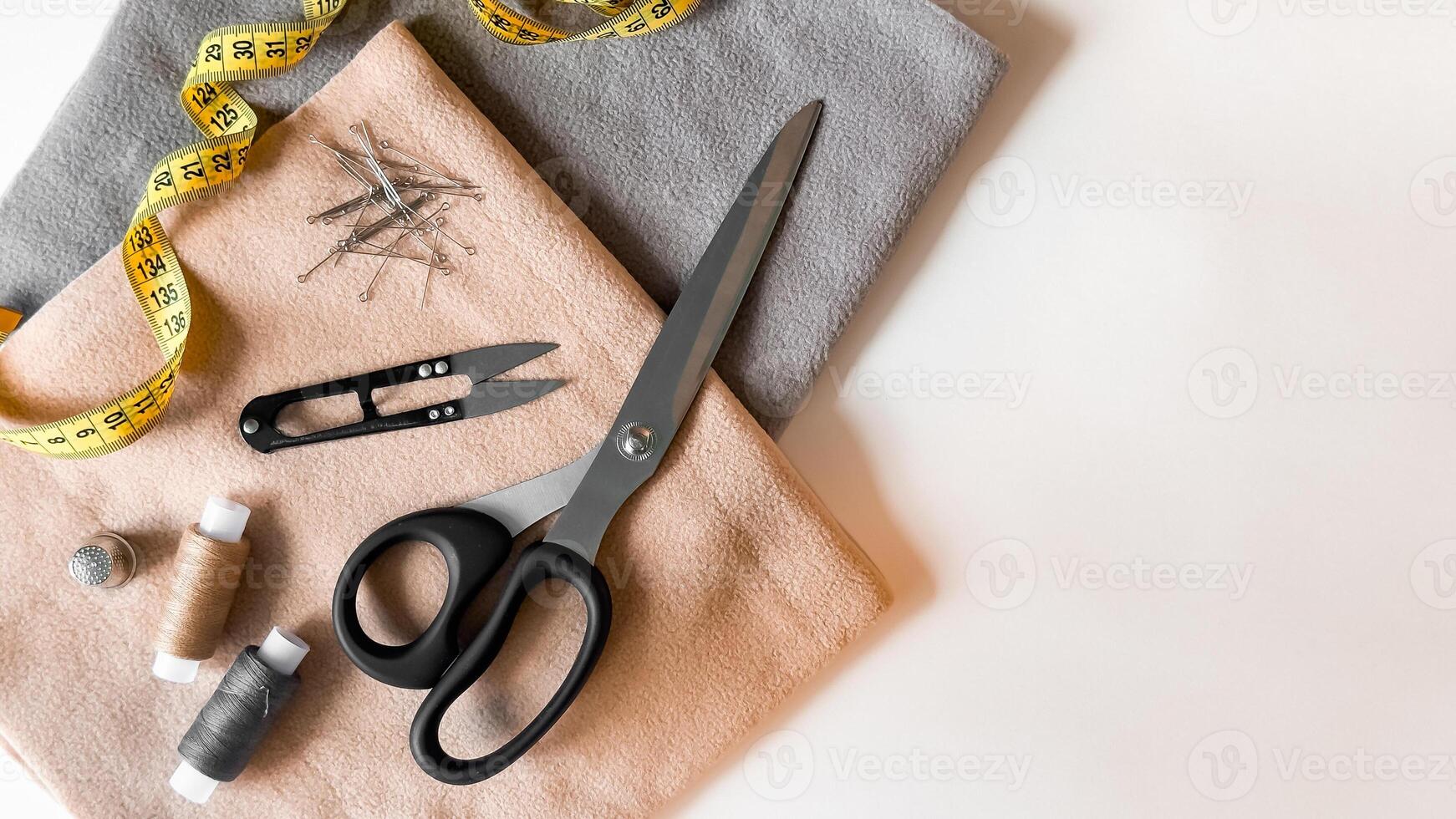 Sewing tools and fabrics. Scissors, thread, measuring tape, needles, and pins on soft cloth photo